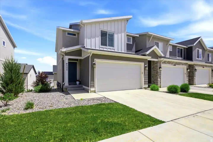 Contemporary exterior featuring a panelized facade, attached two-car garage, concrete driveway, and front door with transom window