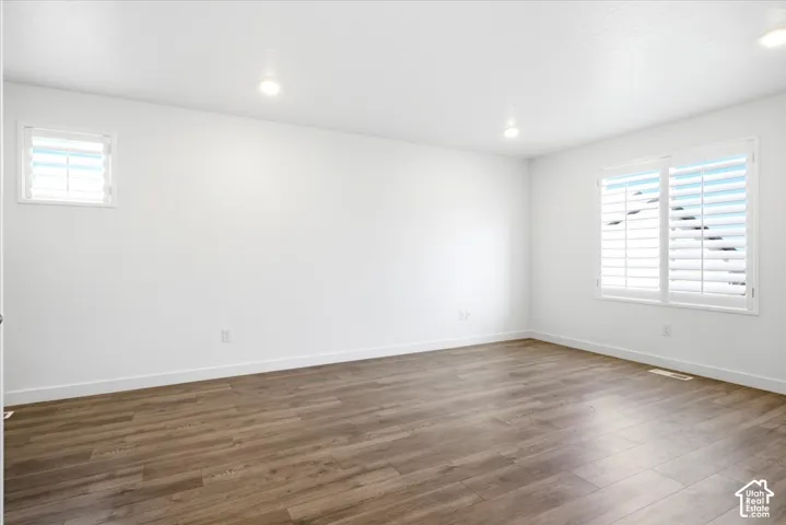 Spacious room featuring wood-finish flooring, white baseboards, and bright white walls