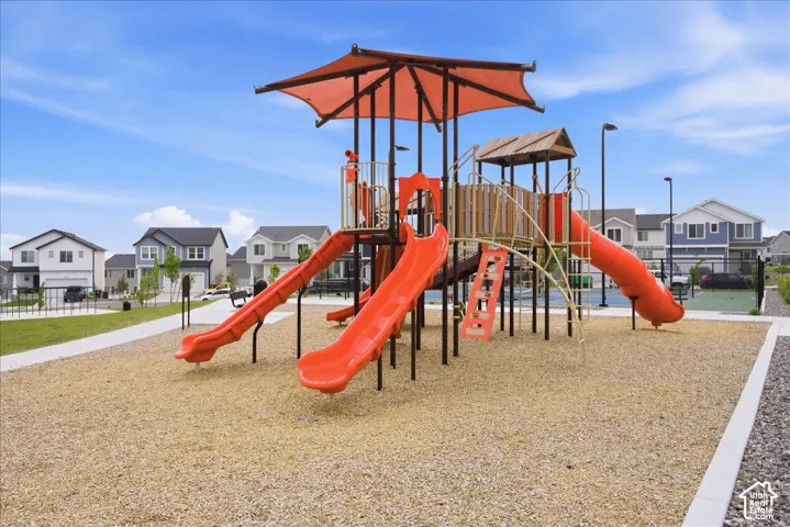 Community playground featuring multiple slides, climbing structures, a protective canopy, and a wood chip surface