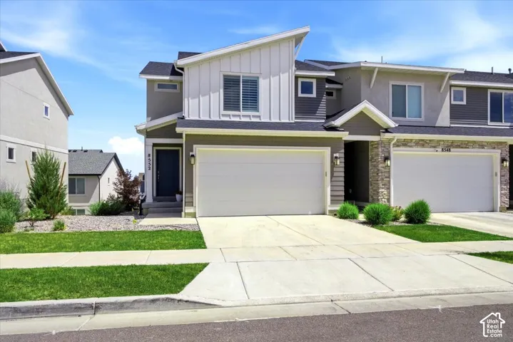 Modern two-story home featuring a clean contemporary exterior with mixed siding materials in neutral tones, peaked rooflines with architectural interest, and a spacious two-car garage with white panel doors