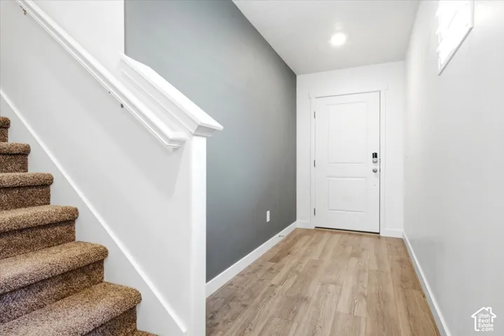 Entryway featuring wood-finish flooring, a white paneled door with hardware, and overhead lighting