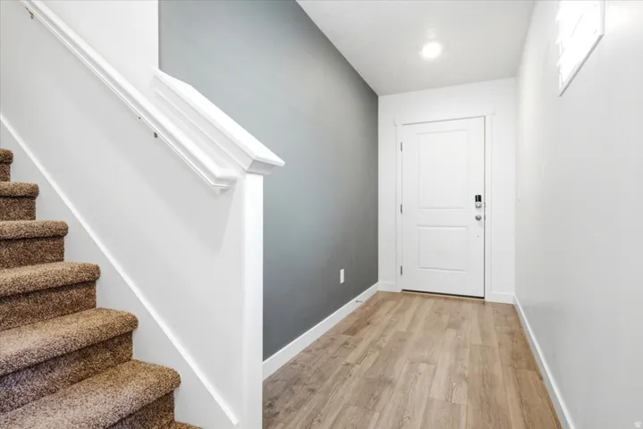 Entryway featuring wood-finish flooring, a white paneled door with hardware, and overhead lighting