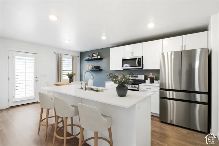 Virtually Enhanced. Kitchen featuring a large island with a countertop, stainless steel appliances, white cabinetry, and wood-finish flooring