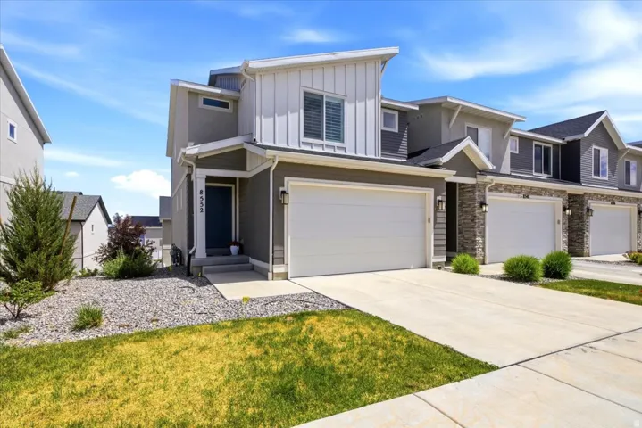 Modern exterior featuring a prominent two-car garage, mixed material facade with vertical siding and stucco, a concrete driveway, and low-maintenance landscaping with decorative rock