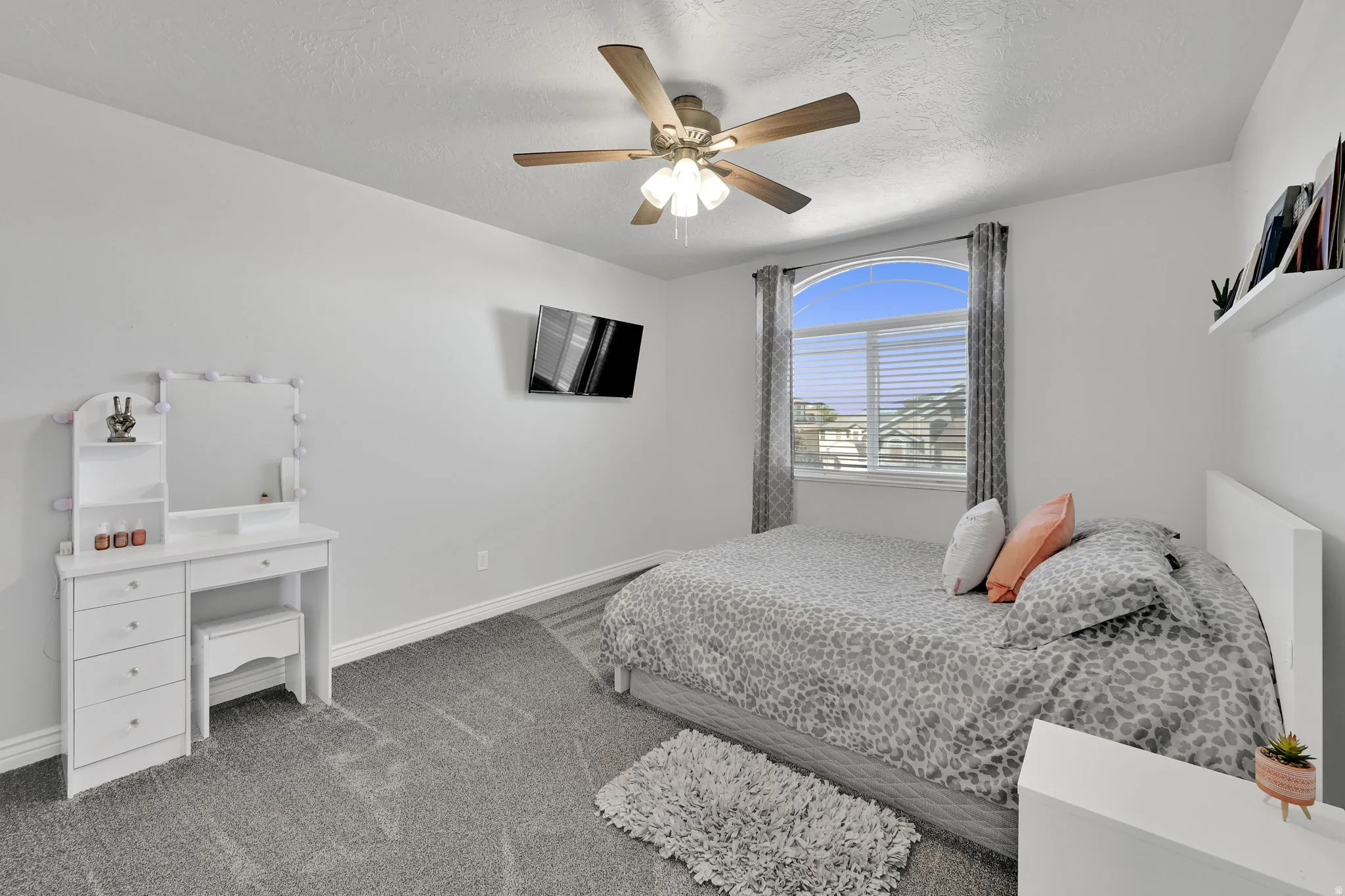 Room featuring gray carpet, a ceiling fan with light fixture, and an arched window with blinds and curtains