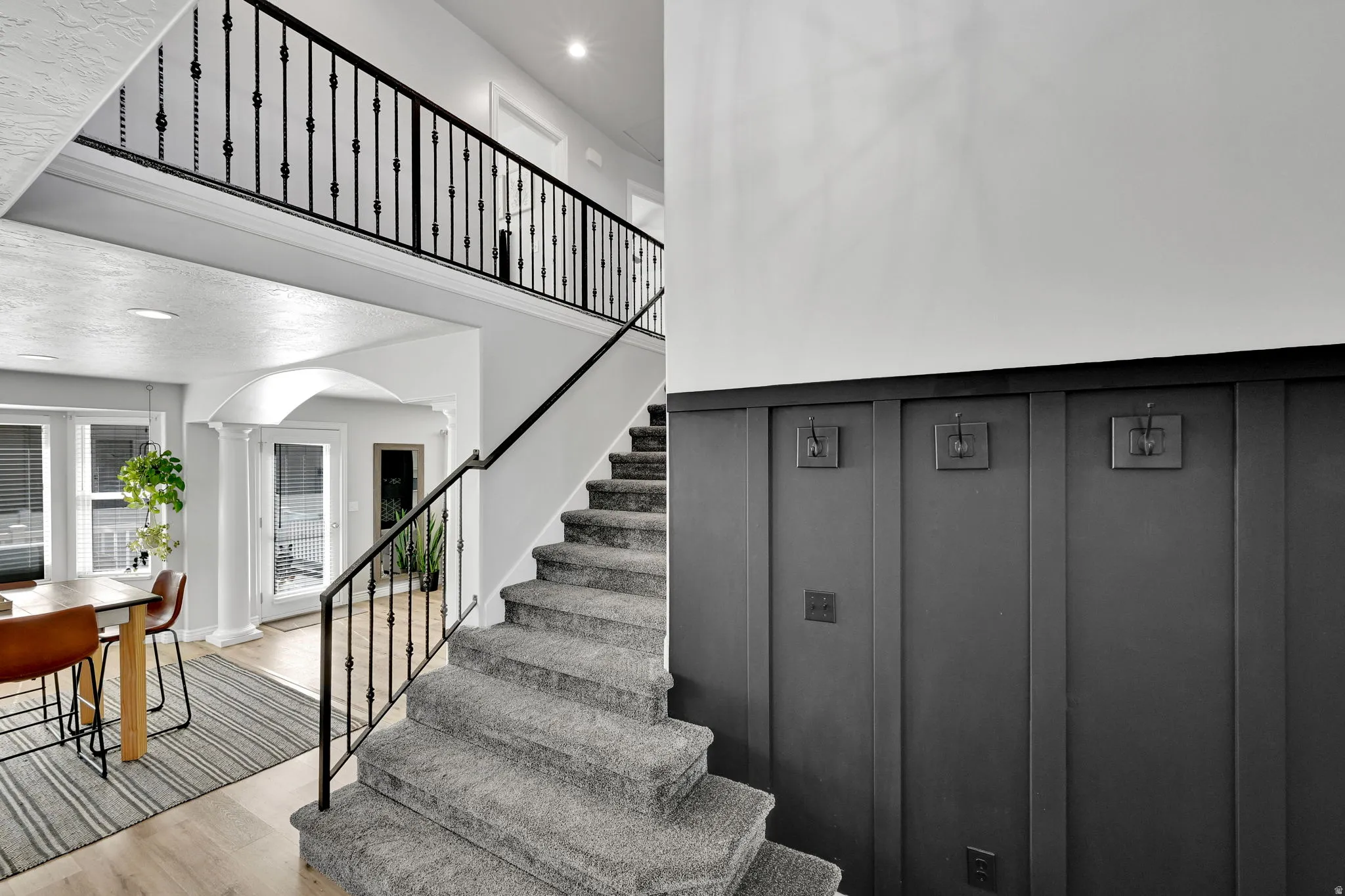 Staircase featuring carpeted treads, a wrought iron railing, and dark wainscoting with integrated wall hooks