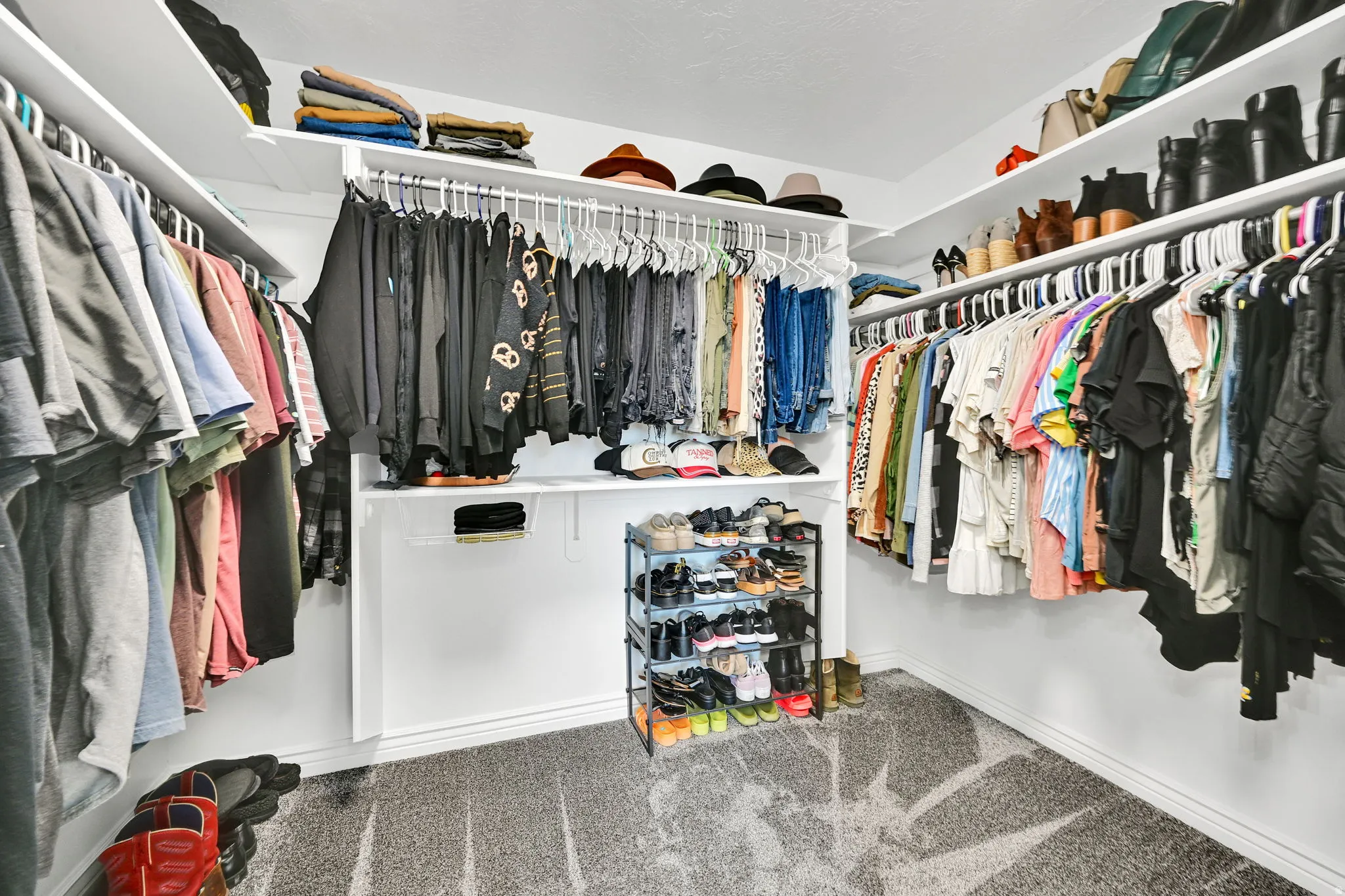 Walk-in closet featuring white built-in shelving, multiple hanging rods, and light gray patterned carpeting