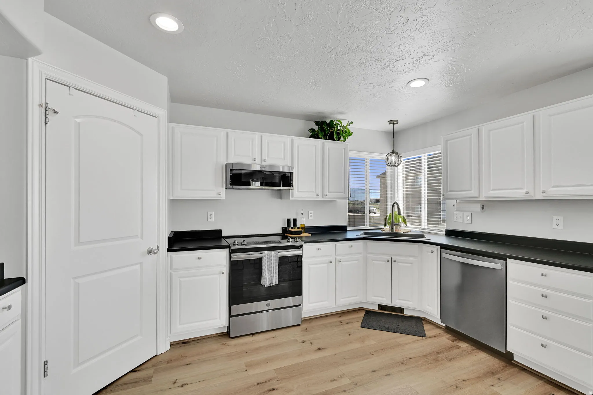 Modern kitchen featuring white cabinetry, dark countertops, stainless steel appliances, wood-finish flooring, and recessed lighting