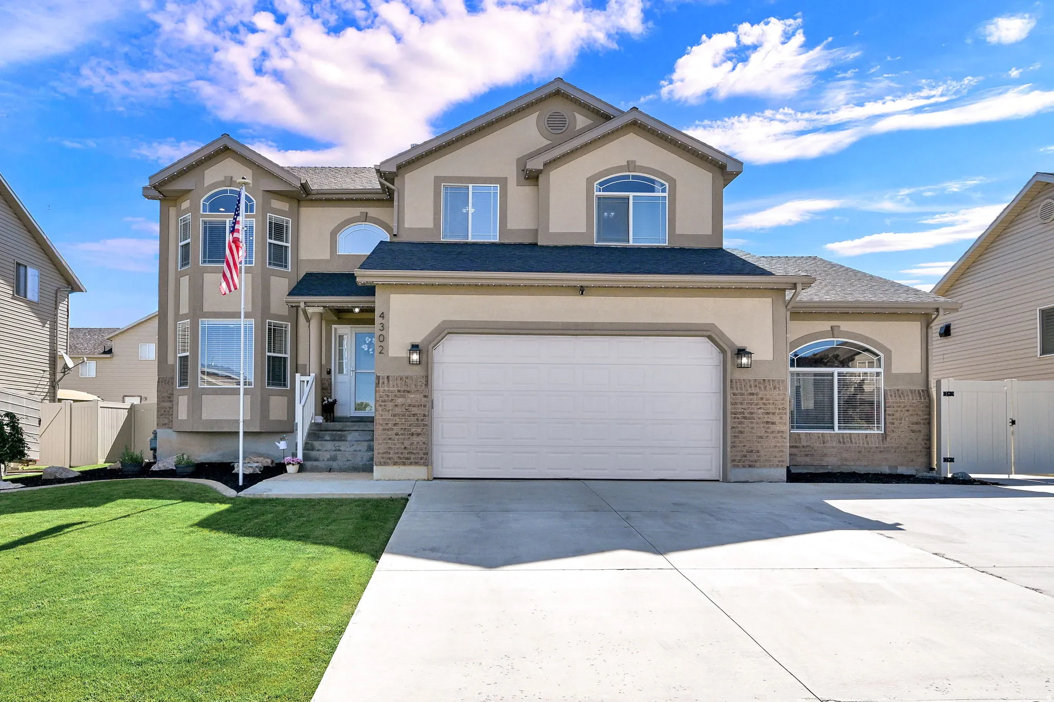 Stucco and brick facade residence featuring a two-car garage, bay window, arched windows, and concrete driveway