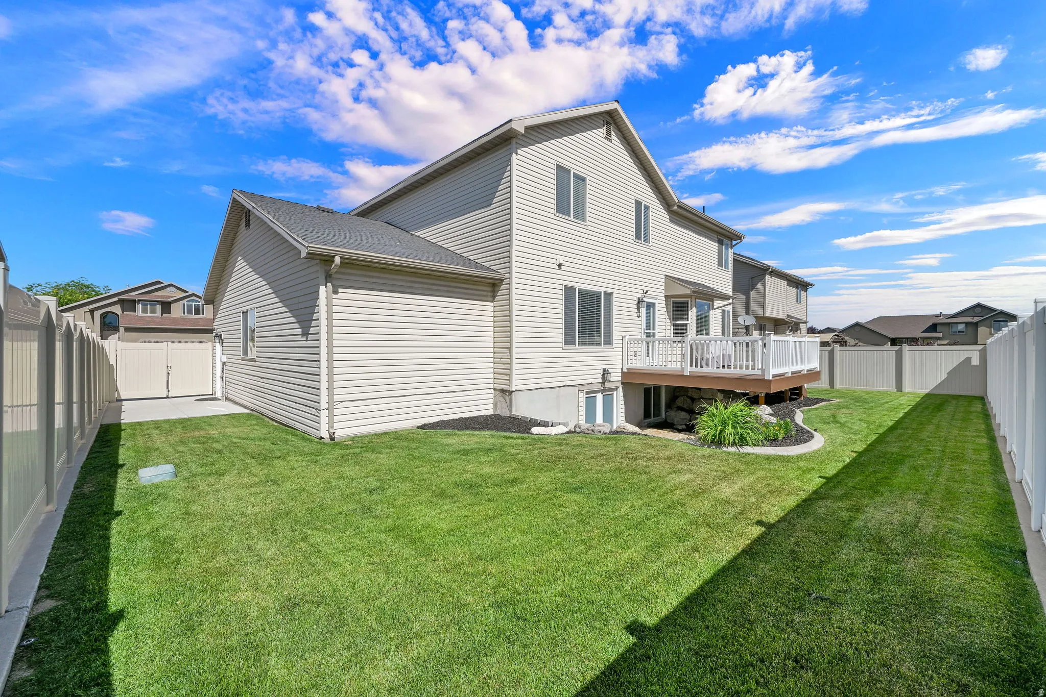 Expansive backyard featuring a manicured lawn, full vinyl fencing, an elevated wood deck with white railing, and a side concrete patio