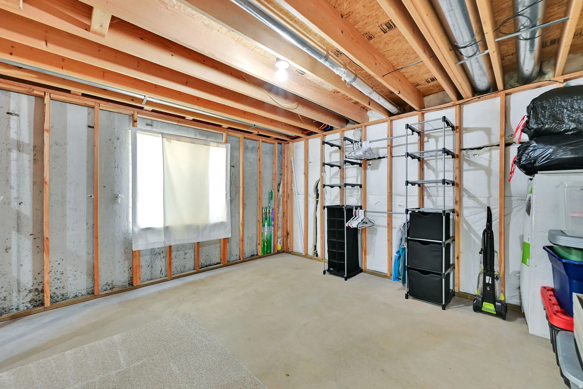 Unfinished basement with exposed wooden framing, concrete walls, and a visible window