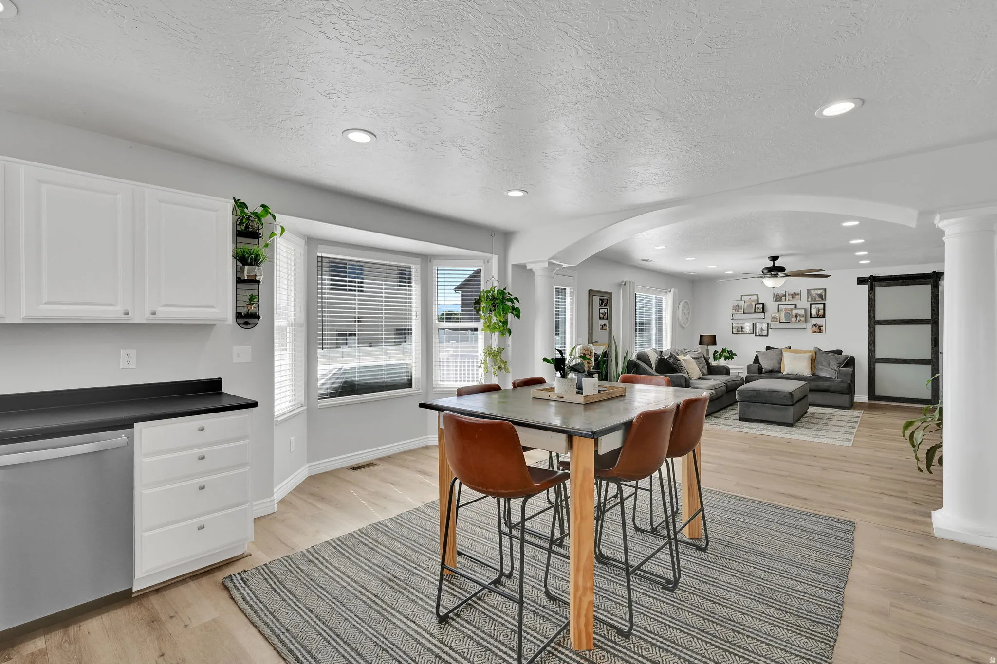 Open-concept living space featuring wood-finish flooring, recessed lighting, and a kitchen area with white cabinetry and dark countertops