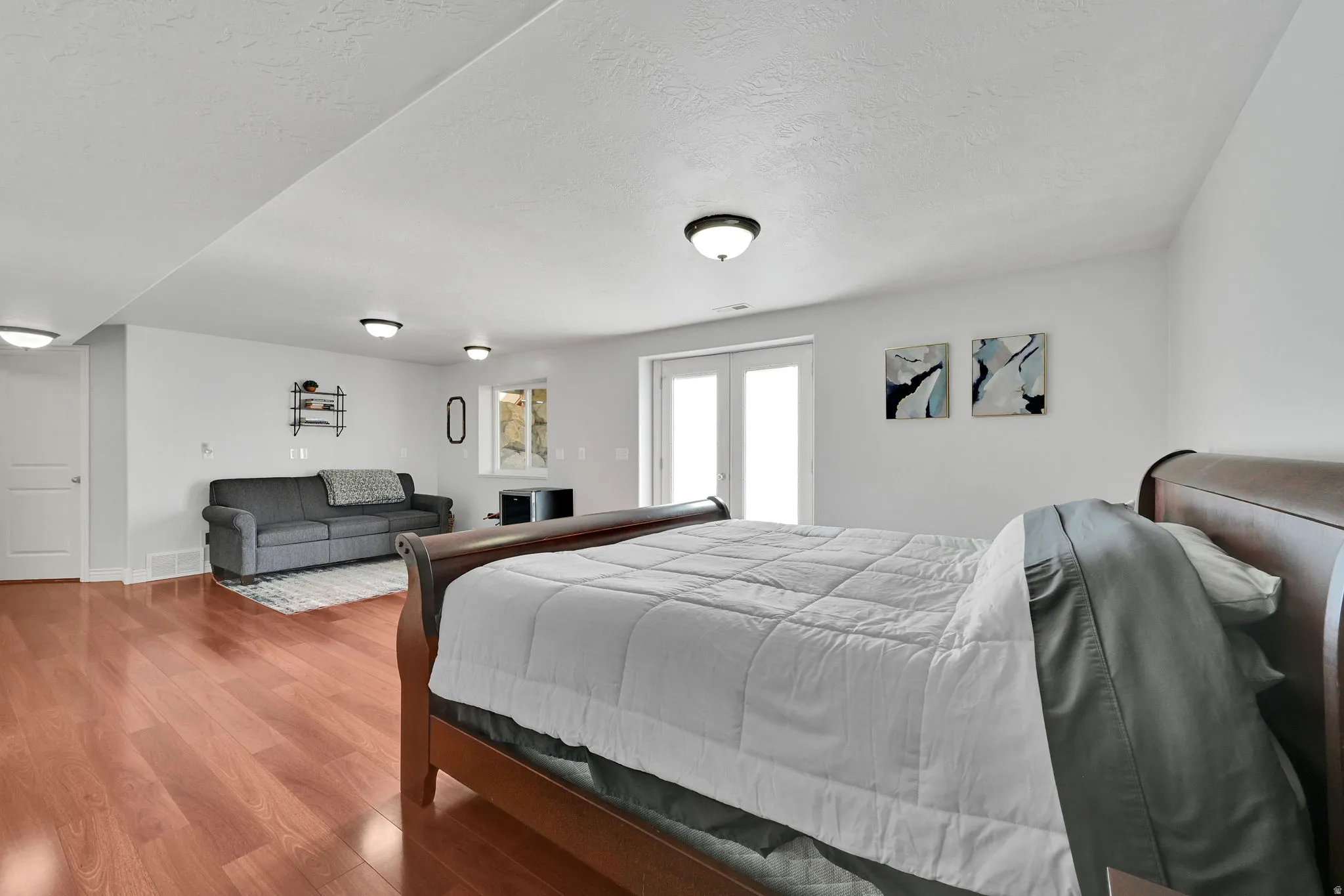 Spacious open-concept room featuring wood-finish flooring, white walls, recessed ceiling lighting, and a double-door exterior entrance