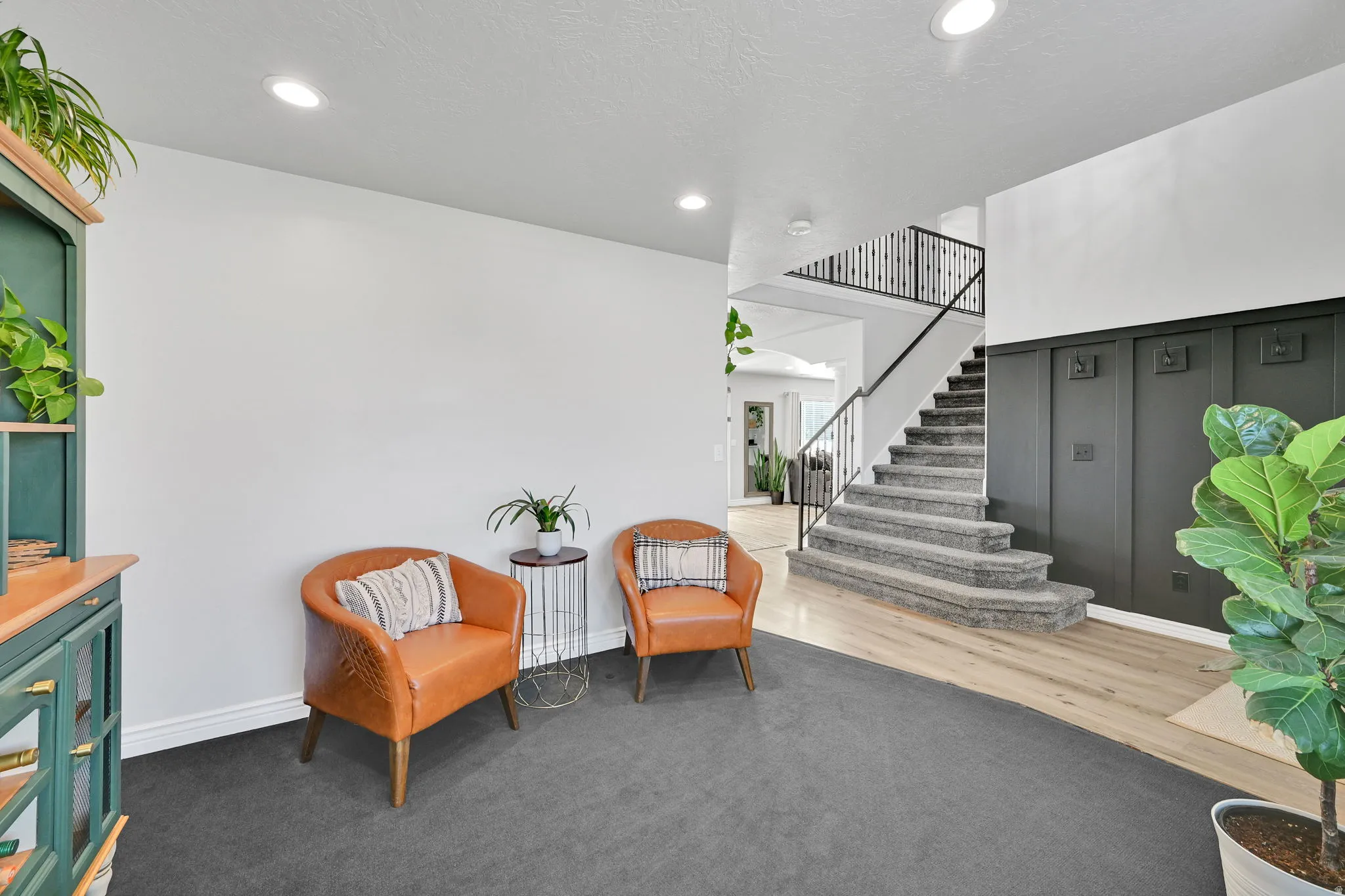 Entryway featuring a carpeted staircase with iron balusters, dark paneled wainscoting, recessed lighting, and wood-finish flooring