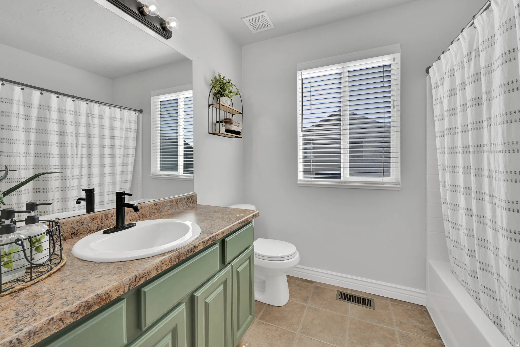 Bathroom featuring a vanity with a green paneled cabinet, an oval undermount sink, and a speckled countertop