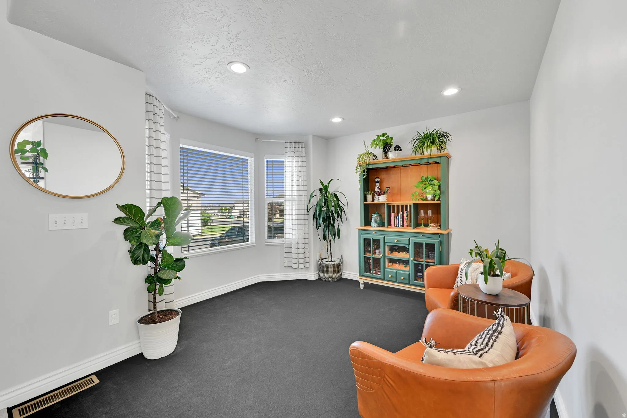 Recessed lighting illuminates the space, featuring large windows with horizontal blinds, perimeter baseboards, and dark carpeting