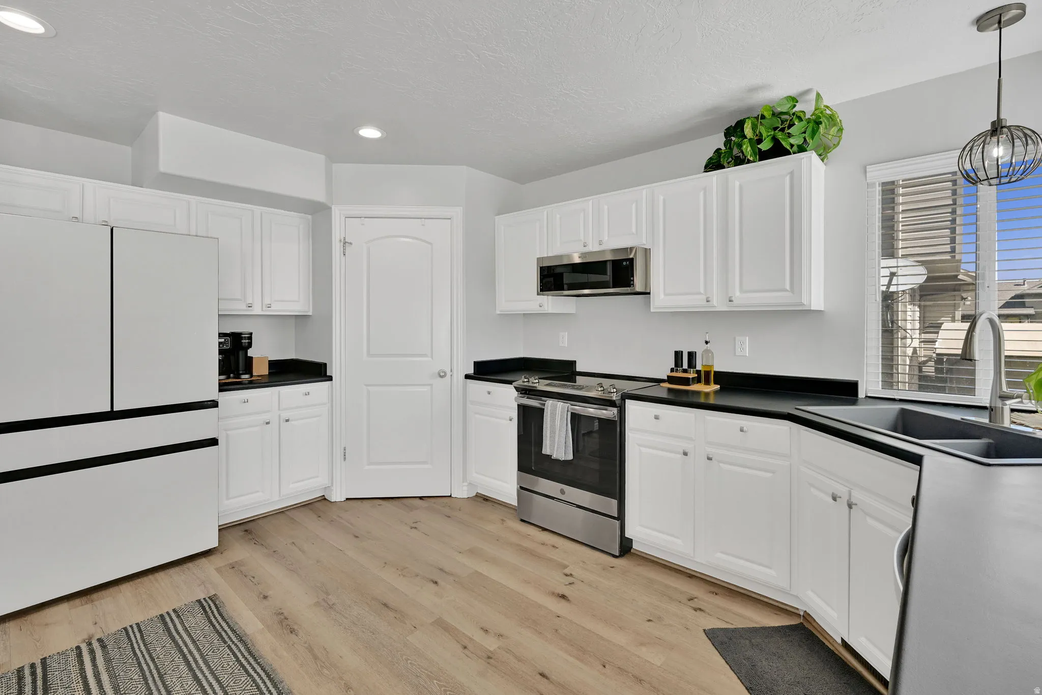 Bright kitchen featuring white cabinetry, dark countertops, wood-finish flooring, stainless steel appliances, and a double basin sink
