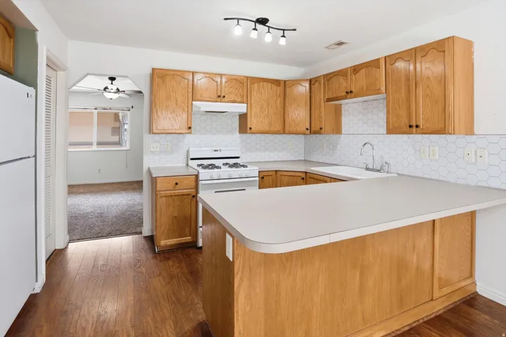 Kitchen featuring wood-finish flooring, light wood cabinetry, white hexagonal tile backsplash, a white gas range, and a breakfast bar with a light-toned countertop