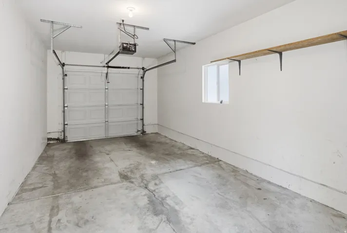 Single-vehicle garage with a panel garage door, concrete flooring, and an automatic garage door opener