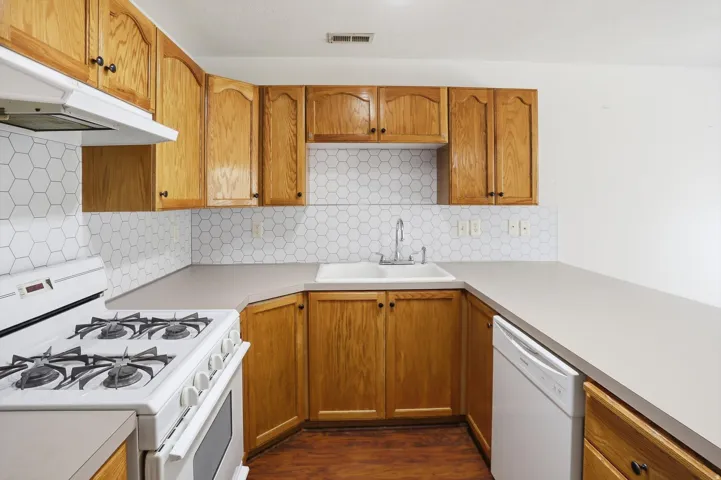 Kitchen featuring wood cabinetry, hexagon tile backsplash, durable countertops, and a white gas range with a matching range hood