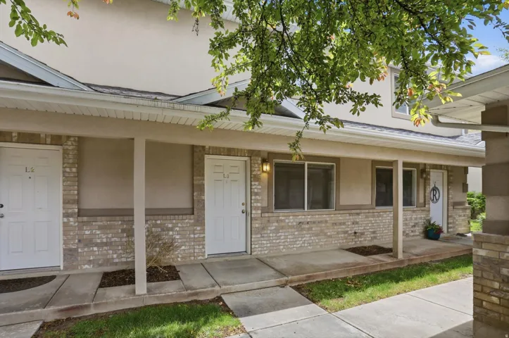 Exterior facade featuring a covered patio, brick detailing, stucco siding, multiple entry doors, and wall-mounted lighting fixtures