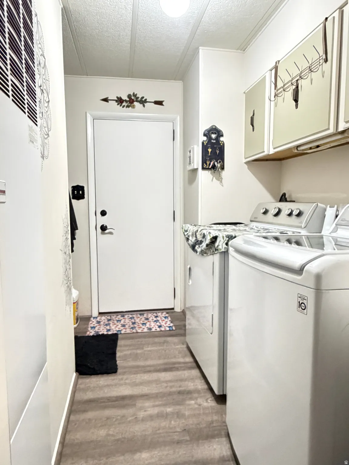 Dedicated laundry area featuring wood-finish flooring, white walls, and built-in upper cabinetry