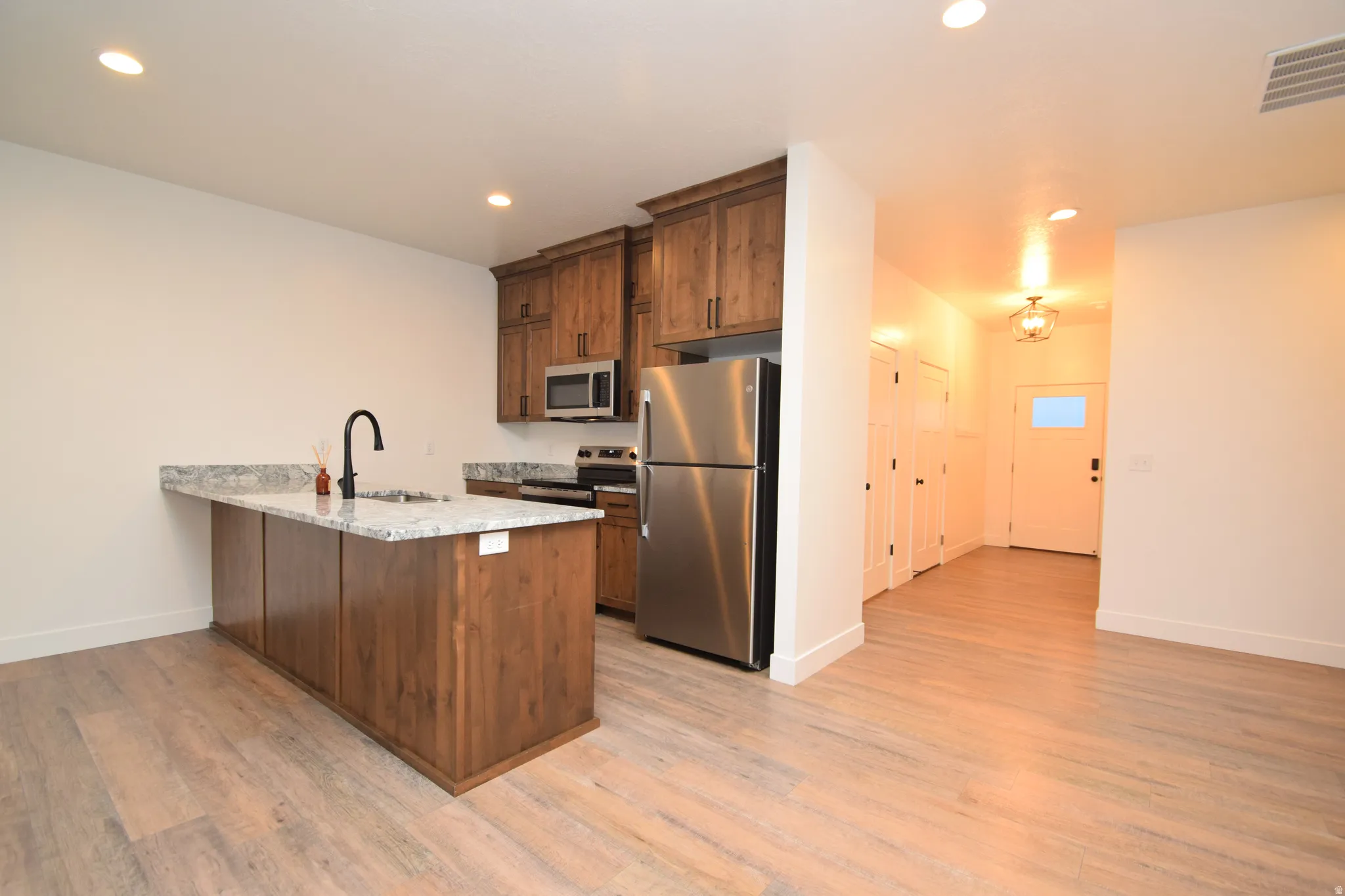 Kitchen featuring an island with a built-in sink, granite countertops, wood-finish cabinetry, stainless steel appliances, and wood-finish flooring