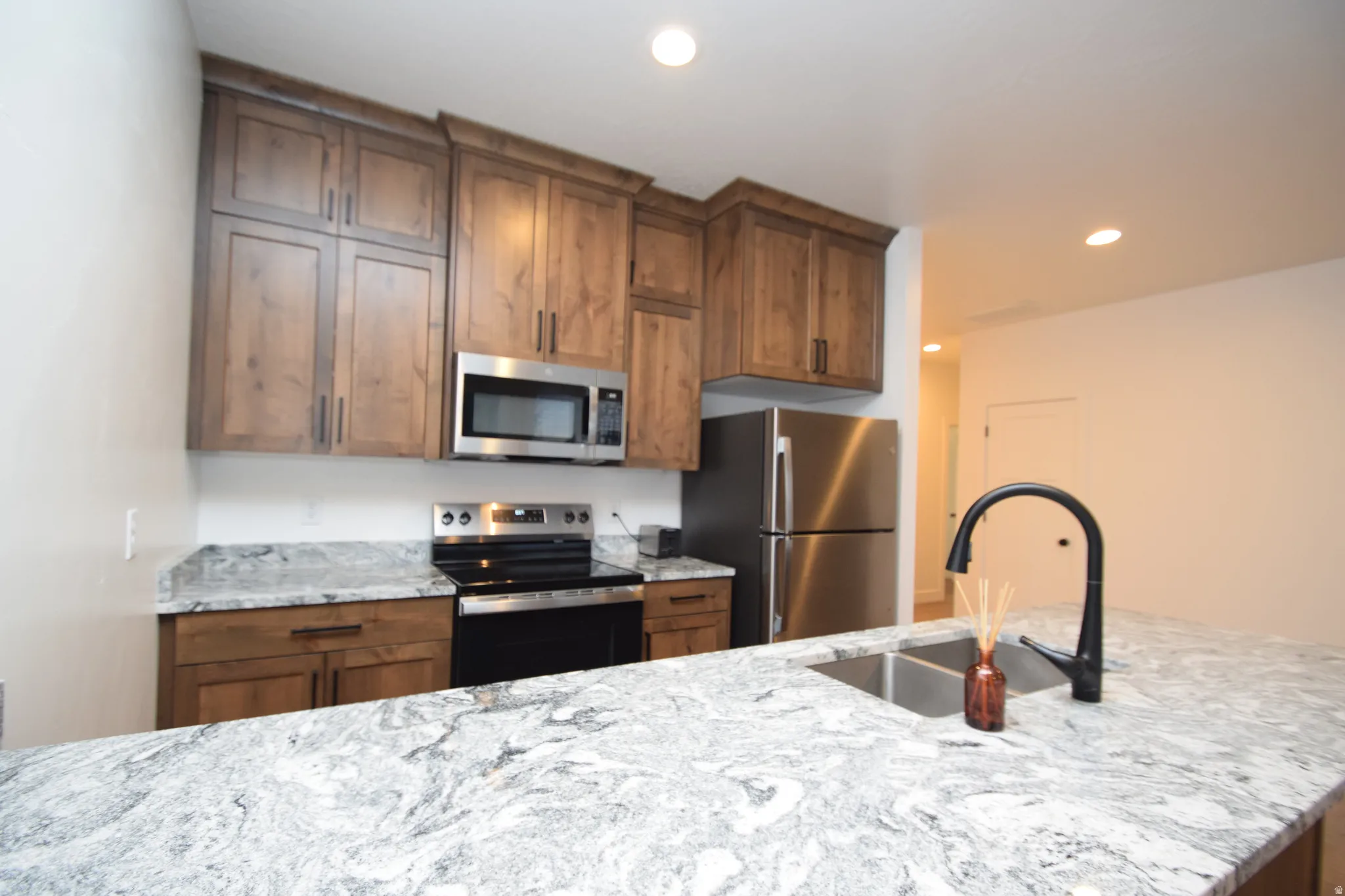 Kitchen featuring wood-finish cabinetry, stainless steel appliances, and ample counter space with a double basin sink and matte black faucet