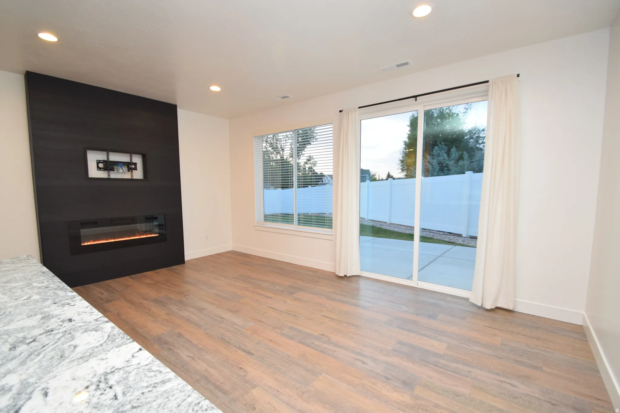 Open-concept living area featuring a contemporary dark wood-paneled fireplace, wood-finish flooring, recessed lighting, and white walls