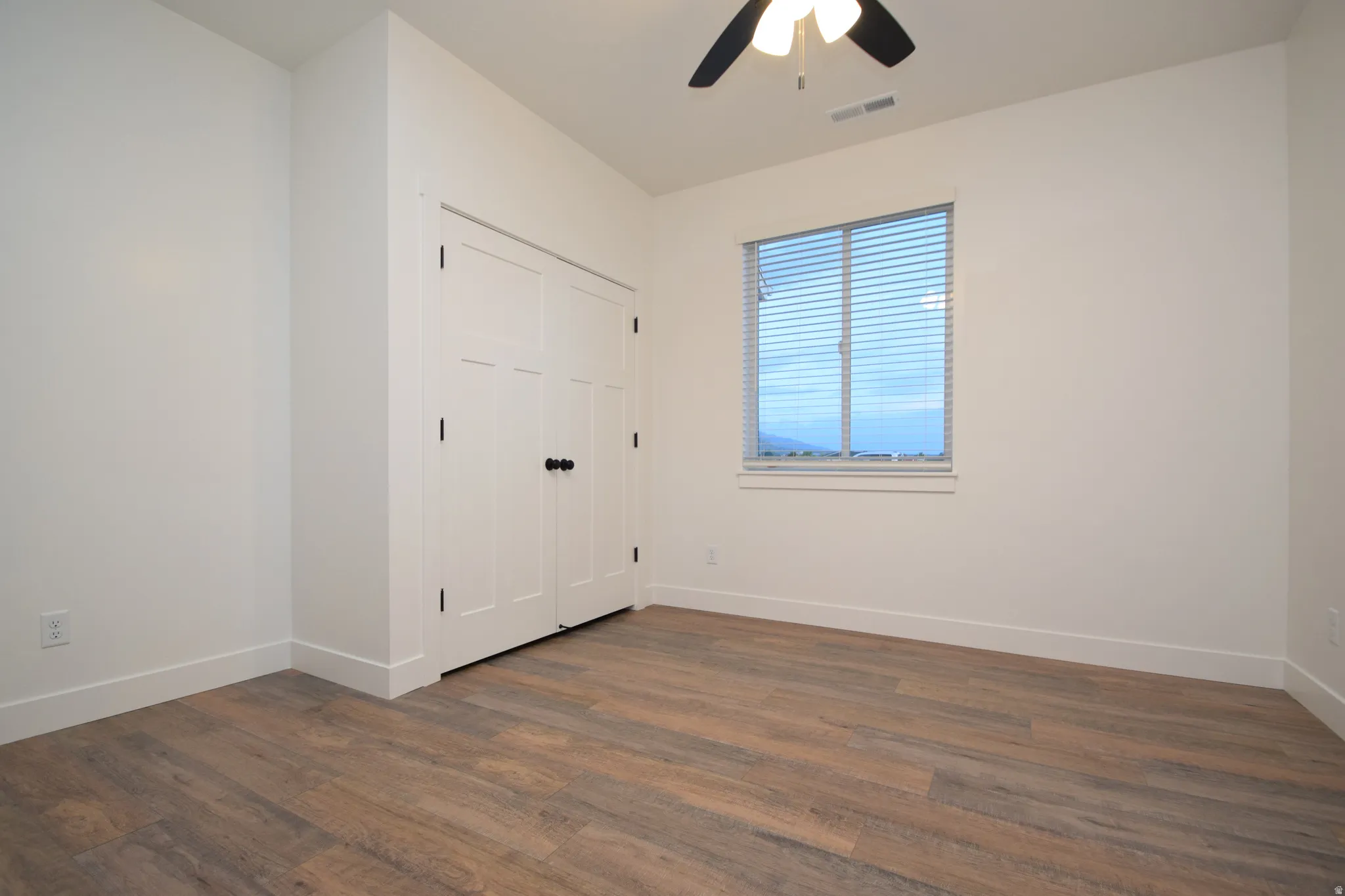 Interior space featuring wood-finish flooring, white walls, and a window with horizontal blinds