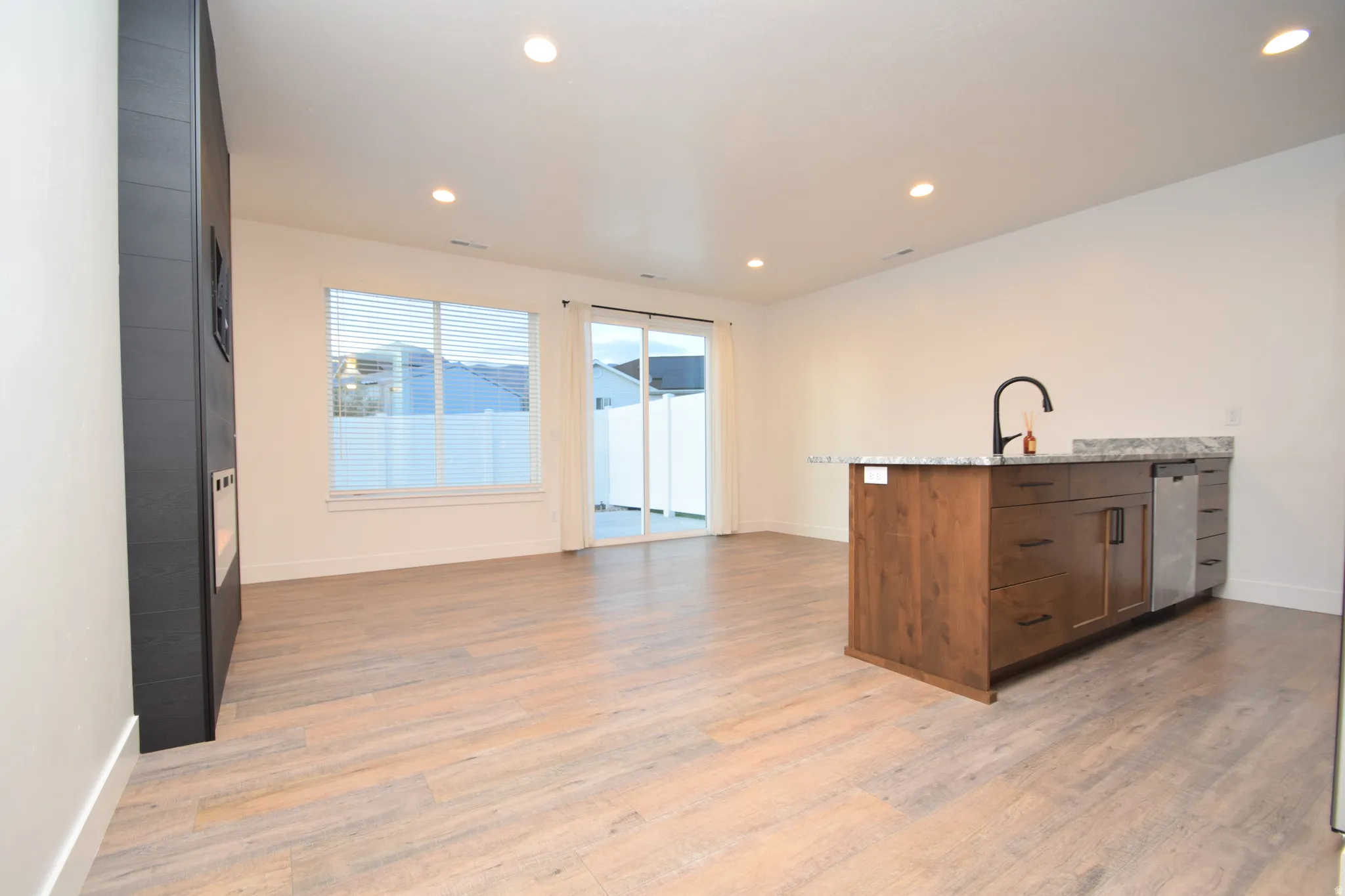 Open-concept living area featuring wood-finish flooring, a contemporary kitchen island with a dark faucet and stone countertop, and recessed lighting