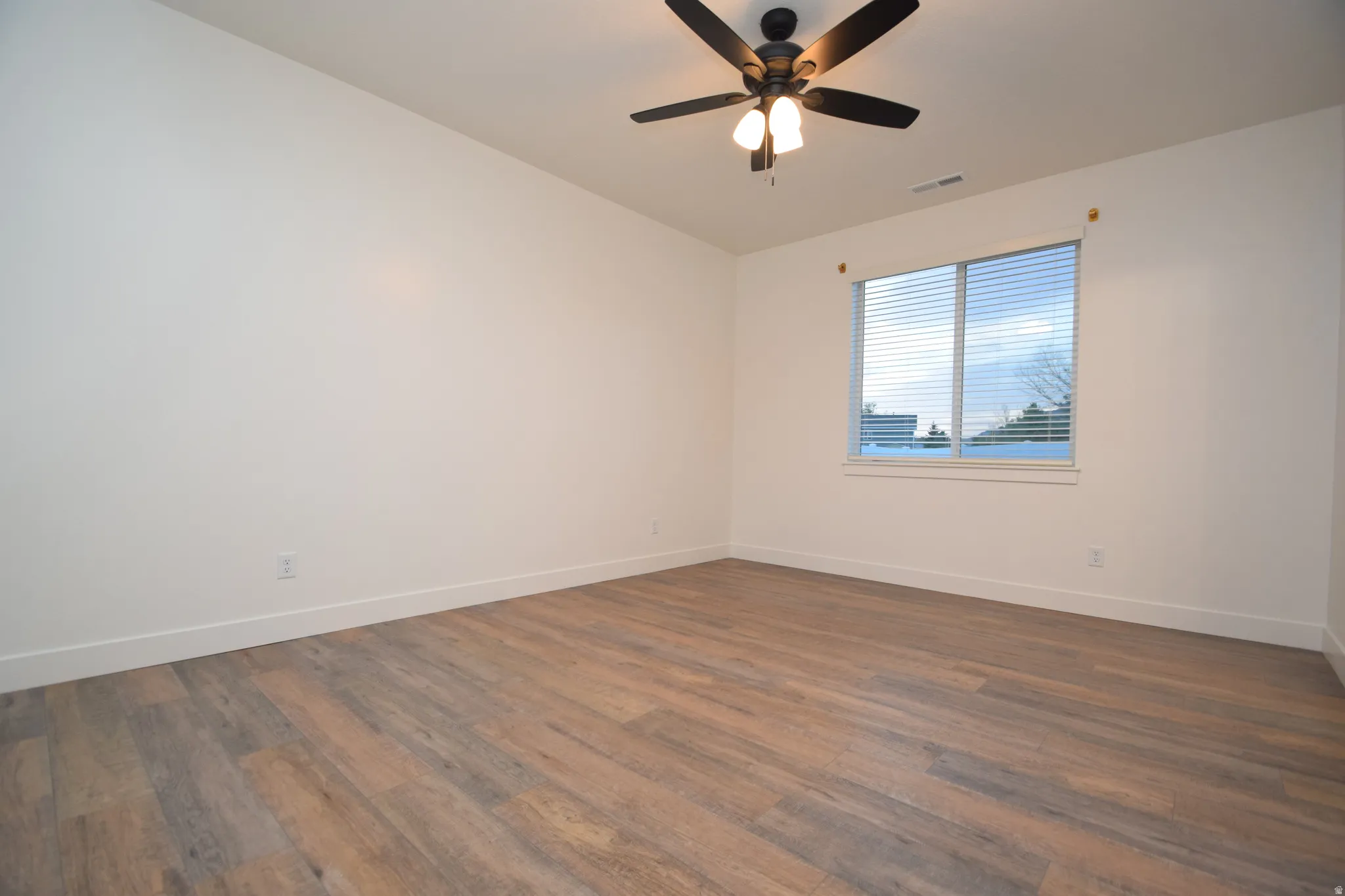 Room featuring wood-finish flooring, white walls, a large window with blinds, and a ceiling fan with integrated lighting