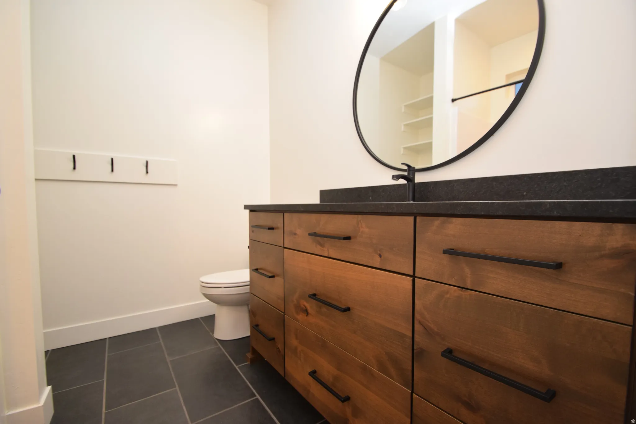 Modern vanity featuring a wood-finish base with abundant storage, black countertop, and matte black fixtures
