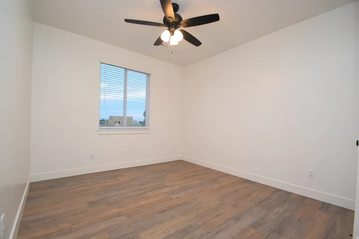 Room featuring wood-finish flooring, white baseboards, and a window with blinds