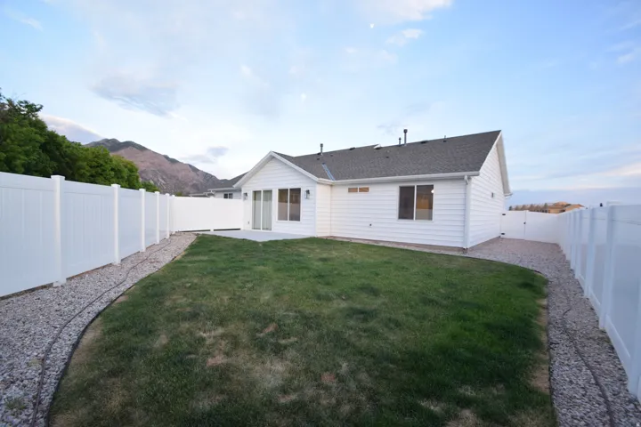 Expansive backyard featuring a manicured lawn, white vinyl fencing, a concrete patio, and gravel borders