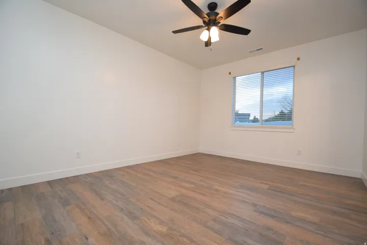 Room featuring wood-finish flooring, white walls, a large window with blinds, and a ceiling fan with integrated lighting