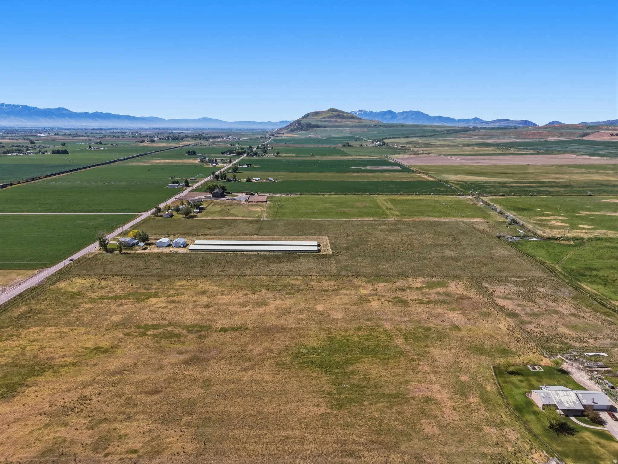 Expansive agricultural property featuring multiple fields, a long paved road, and distant mountain ranges