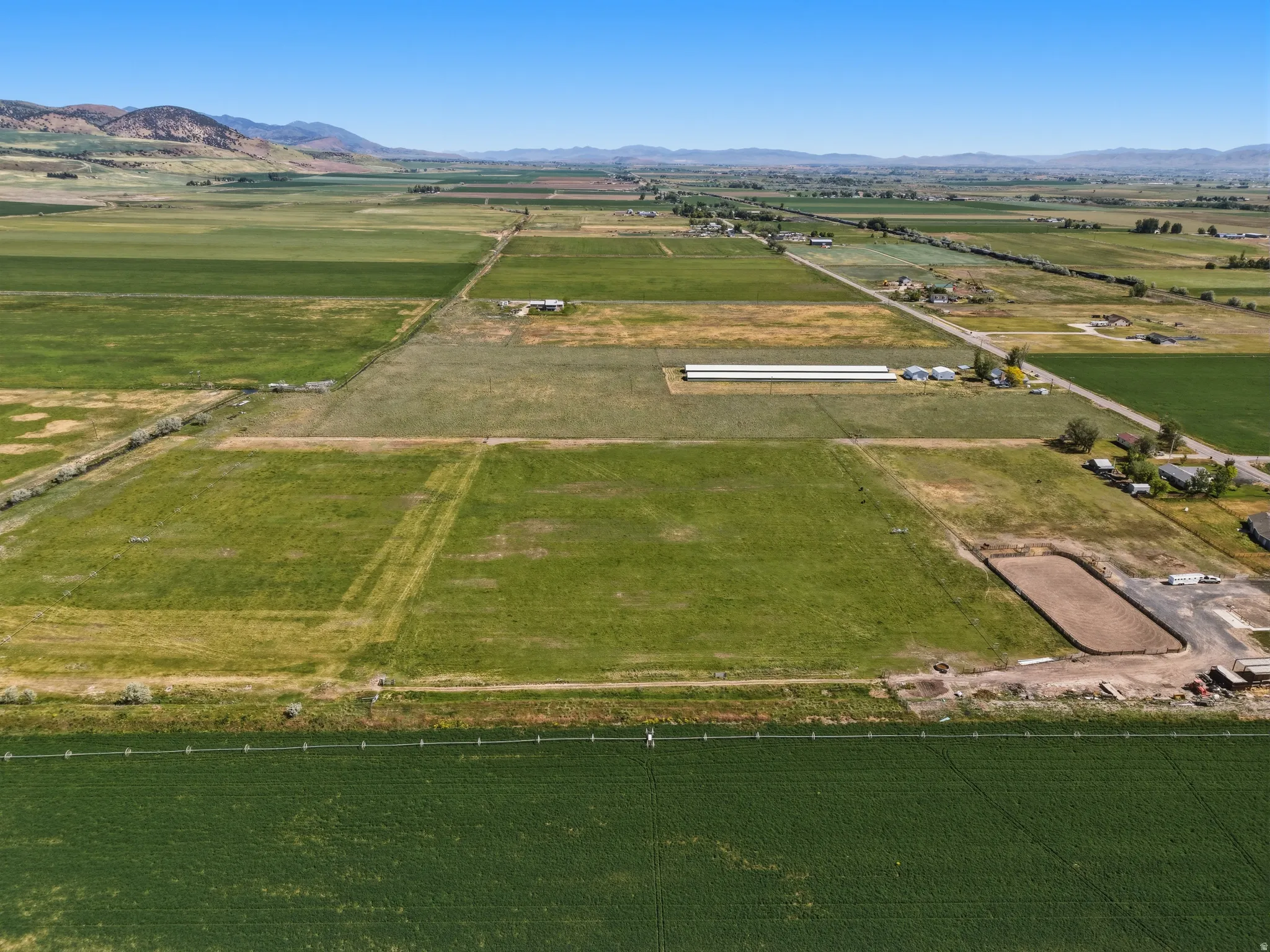 Expansive agricultural land featuring a large, level riding arena, multiple outbuildings, and distant mountain ranges