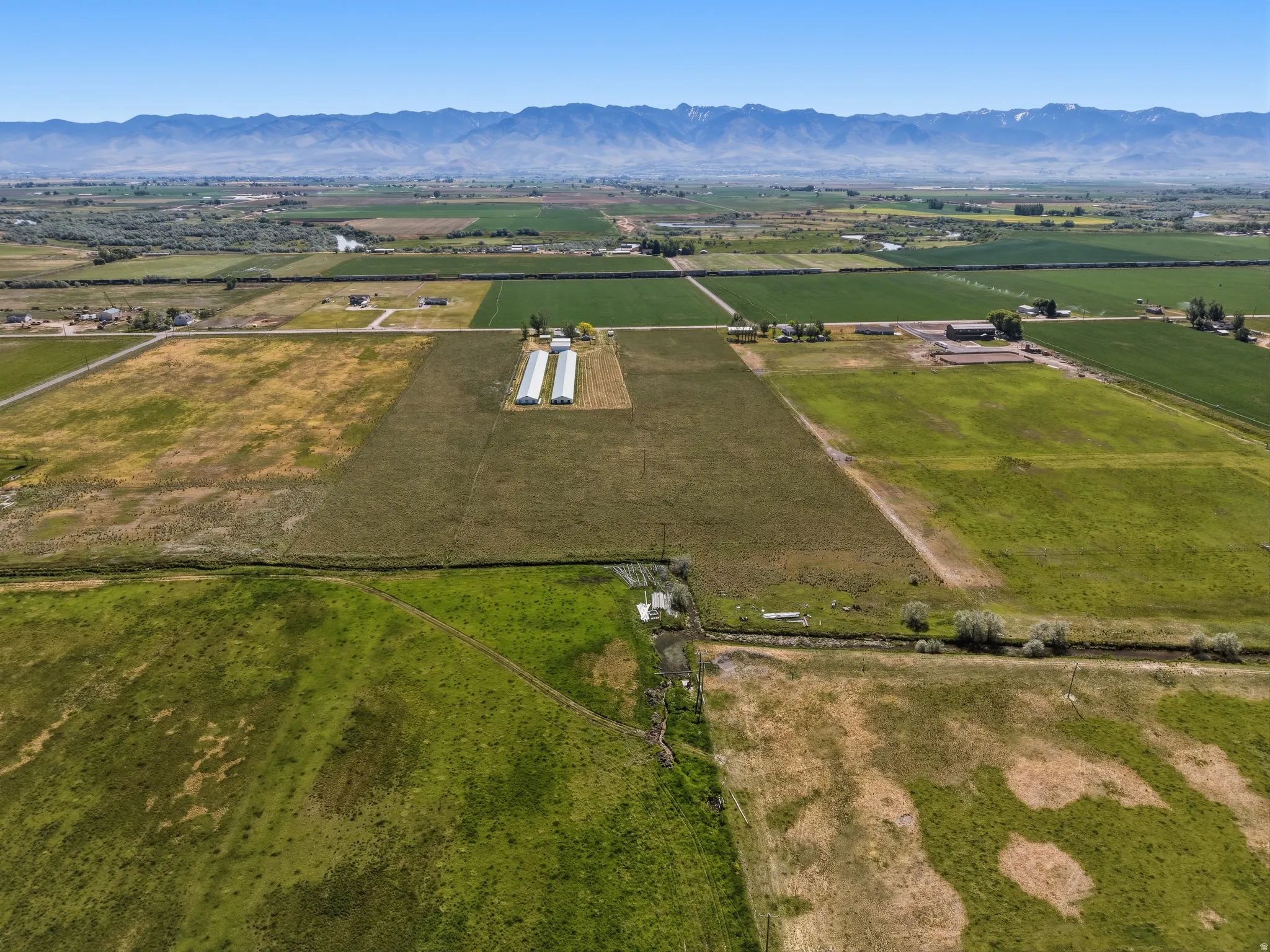 Expansive agricultural property featuring multiple cultivation fields, two large greenhouses, and a distant mountain backdrop