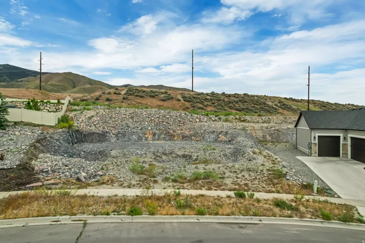 Excavated lot with a prepared building pad and surrounding rocky terrain, featuring a paved street frontage and distant rolling hills