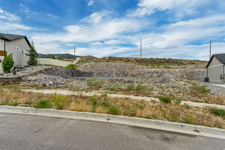Expansive undeveloped lot featuring a gradual slope, natural rock formations, and a paved street frontage