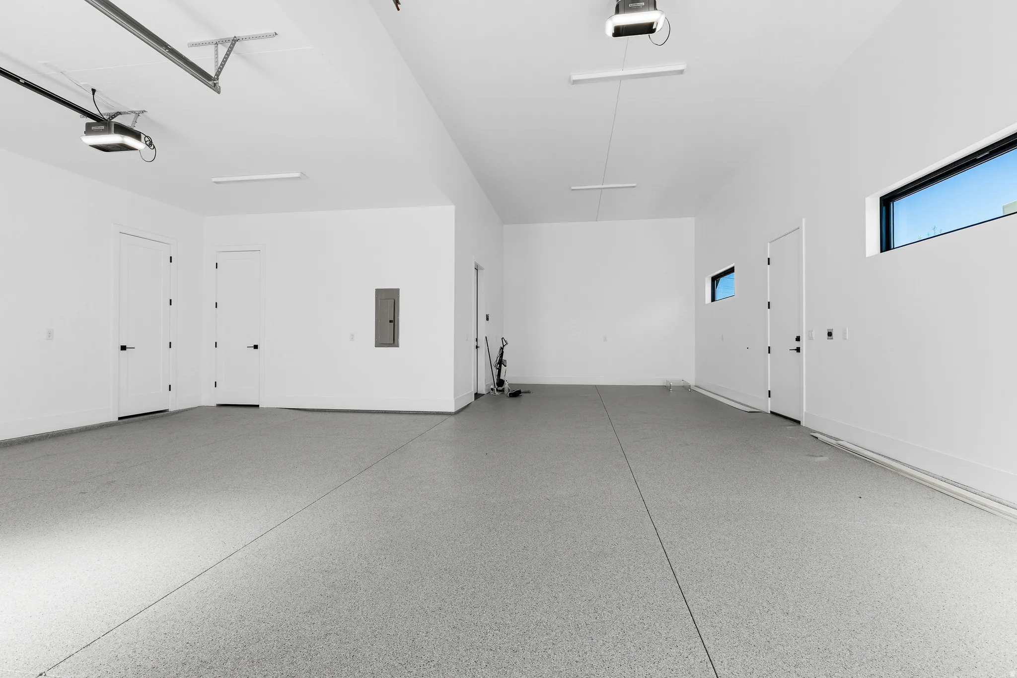 Spacious garage featuring a light gray speckled epoxy floor, multiple entry doors, transom windows, and built-in lighting