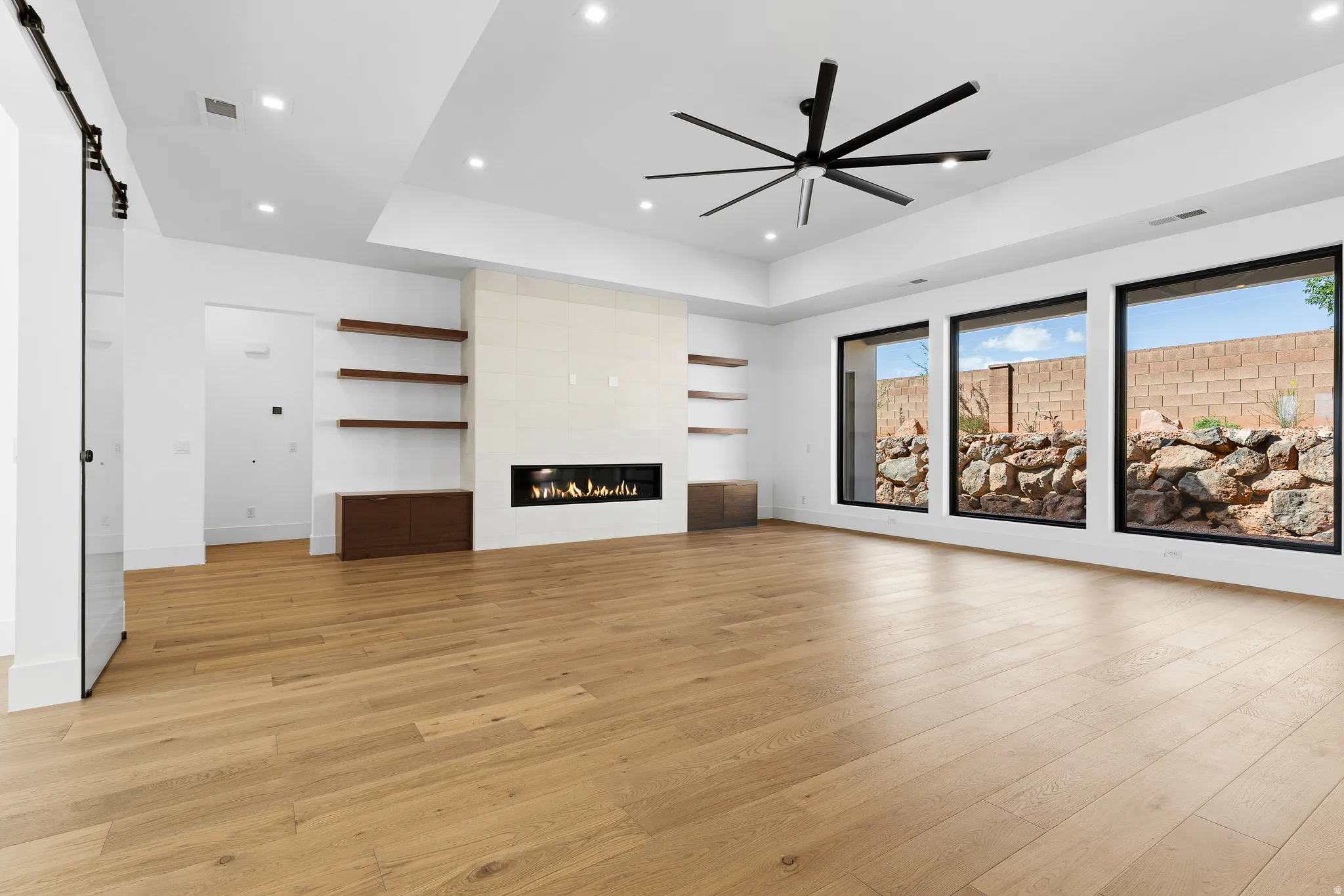 Spacious living area featuring wood-finish flooring, a linear fireplace with a textured surround, and a ceiling fan