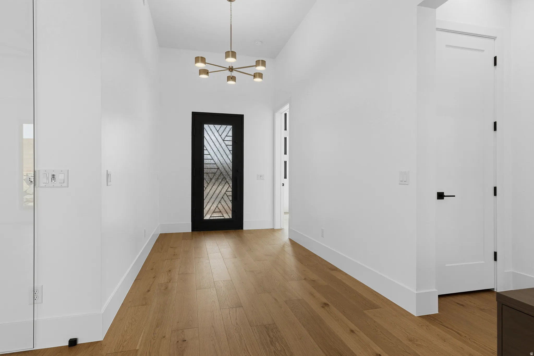 Foyer featuring a modern chandelier, a black door with patterned glass, wood-finish flooring, white walls, and contemporary baseboards