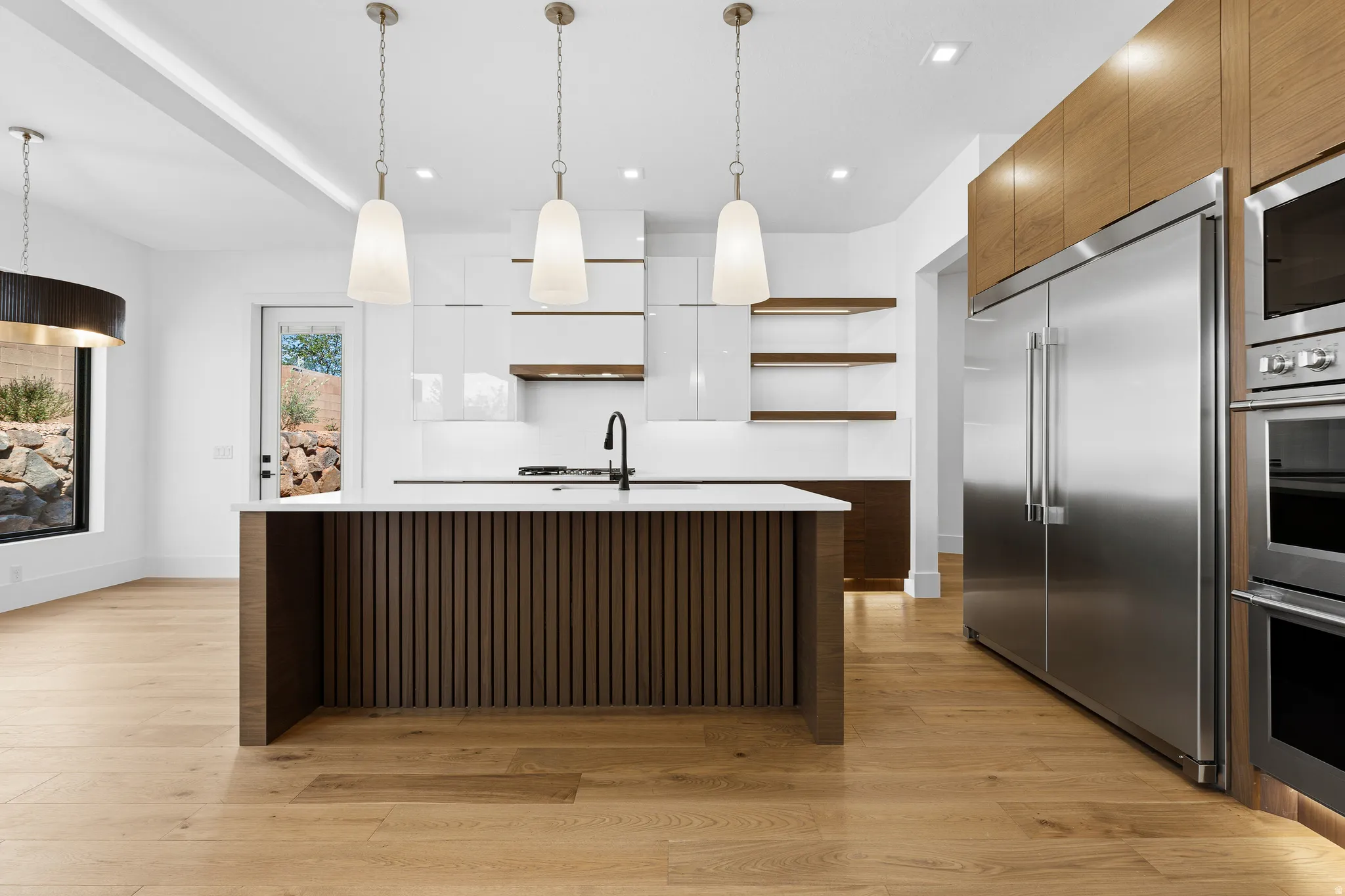 Gourmet kitchen featuring a slatted wood-finish island with white countertop, integrated gas cooktop, sleek white cabinetry, and stainless steel appliances