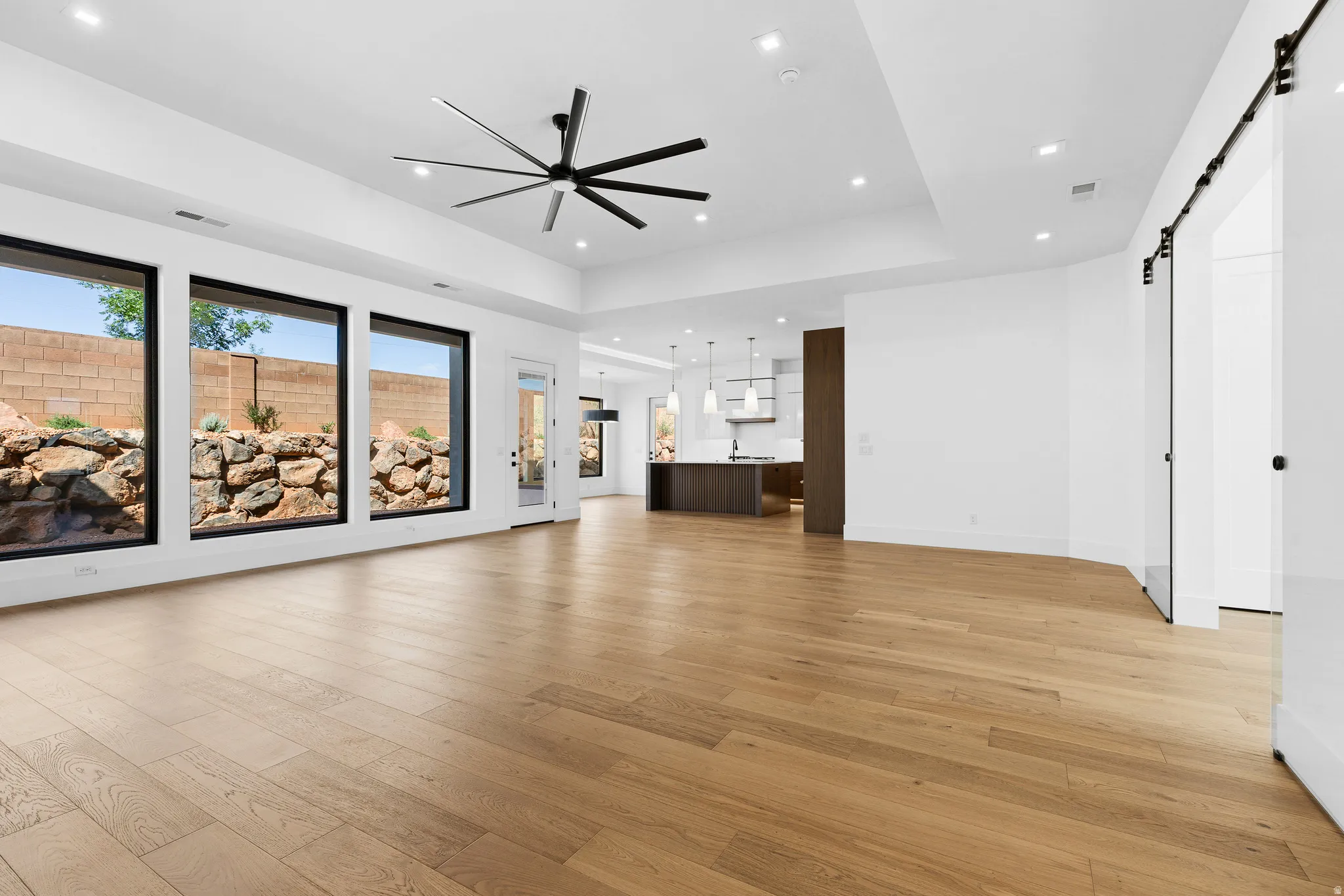 Spacious living area featuring light wood-finish flooring, a contemporary ceiling fan, and recessed lighting