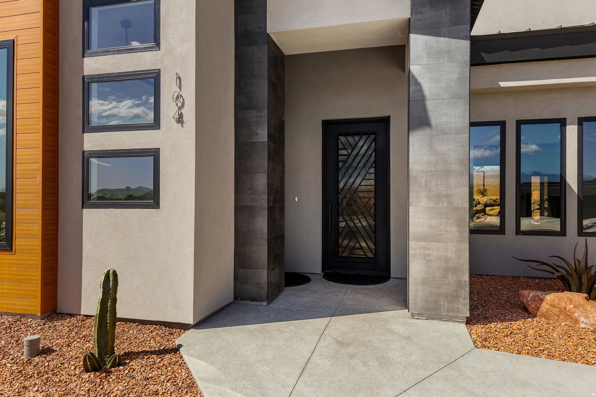 Contemporary exterior featuring a textured stucco finish, dark metal-framed windows, and wood-finish siding