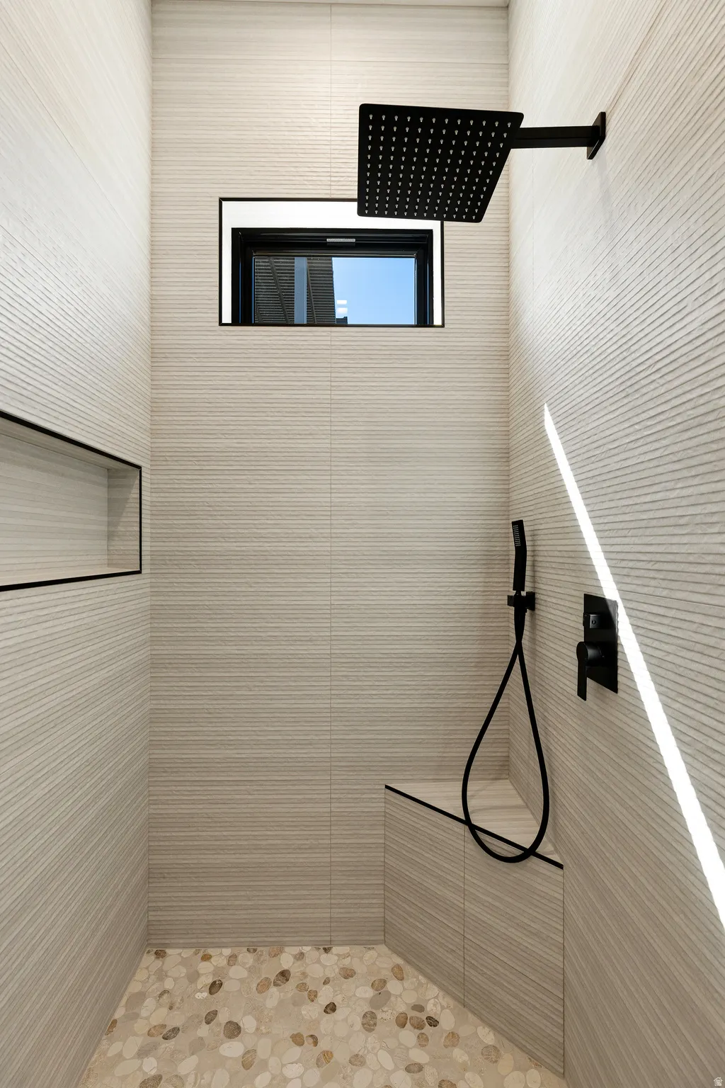 Contemporary shower stall featuring textured tile walls, a built-in bench, and a pebble-finish floor