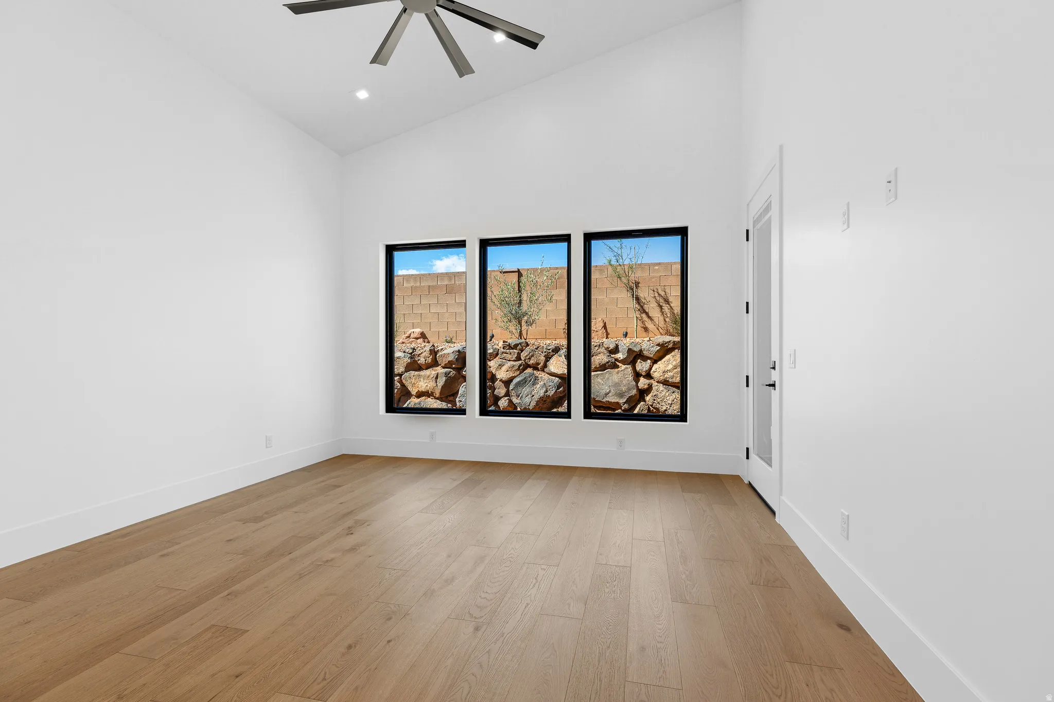 Vaulted ceiling with a contemporary ceiling fan, three vertical windows with black trim, wood-finish flooring, recessed lighting, and a white interior door with frosted glass