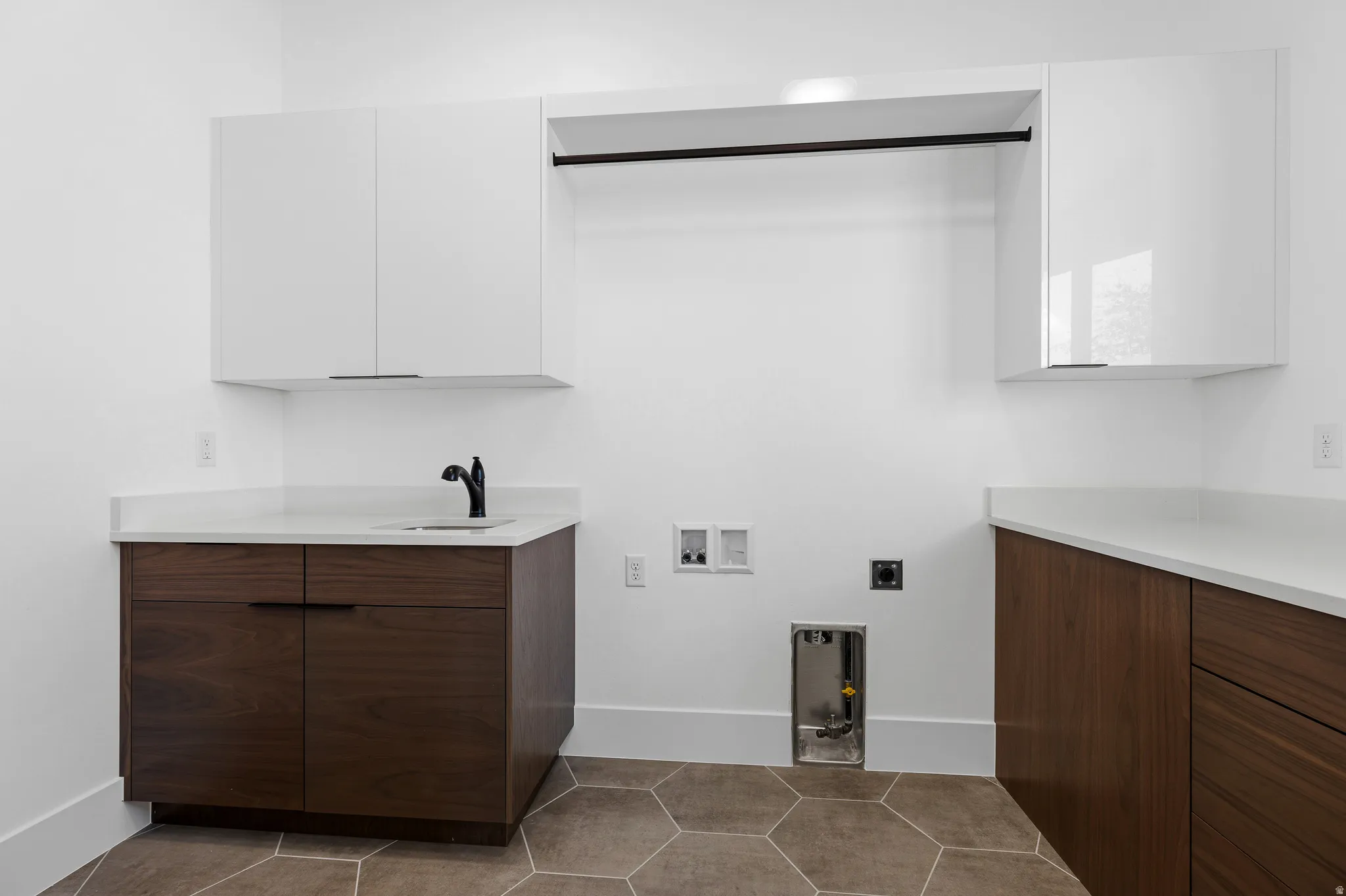 Utility room featuring hexagonal floor tiles, white walls, and a combination of white upper cabinetry and wood-finish lower cabinetry